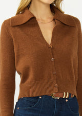 [Color: Brown] A detail image of a blonde model wearing a brown cropped sweater with a wide collar, button front, and ribbed trim. Styled with a dark was denim. 