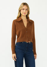 [Color: Brown] A front facing image of a brunette model wearing a brown cropped sweater with a wide collar, button front, and ribbed trim. Styled with a dark was denim. 