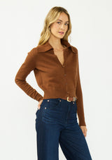 [Color: Brown] A side facing image of a blonde model wearing a brown cropped sweater with a wide collar, button front, and ribbed trim. Styled with a dark was denim. 