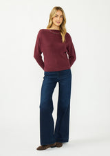 [Color: Oxblood] A front facing image of a blonde model wearing a burgundy pullover sweater with a boat neckline and long sleeves that taper at the cuffs. 