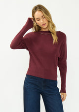 [Color: Oxblood] A front facing image of a blonde model wearing a burgundy pullover sweater with a boat neckline and long sleeves that taper at the cuffs. 