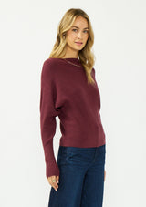 [Color: Oxblood] A side facing image of a blonde model wearing a burgundy pullover sweater with a boat neckline and long sleeves that taper at the cuffs. 