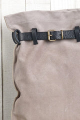 [Color: Sand/Nero] A detail image of a light grey suede pouch backpack with an adjustable belt closure and leather shoulder straps. 