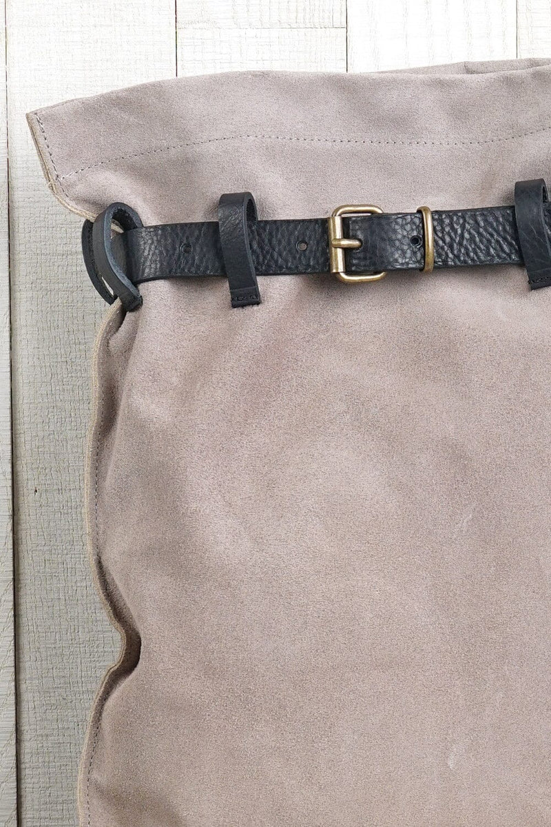 [Color: Sand/Nero] A detail image of a light grey suede pouch backpack with an adjustable belt closure and leather shoulder straps. 