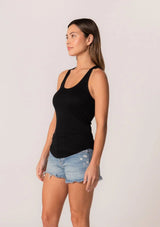 [Color: Black] A half body side facing image of a brunette model wearing a classic slim fit stretchy knit black tank top with a scoop neckline and racerback.