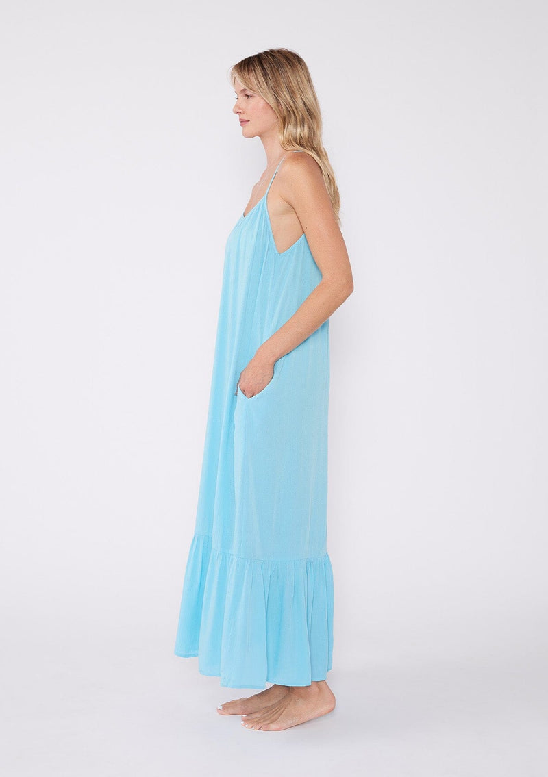 [Color: Aqua] A side facing image of a blonde model wearing an aqua blue bohemian sleeveless maxi dress. With spaghetti straps, a scoop neckline, side pockets, a long flowy tiered skirt, and a sheer lace racerback detail.