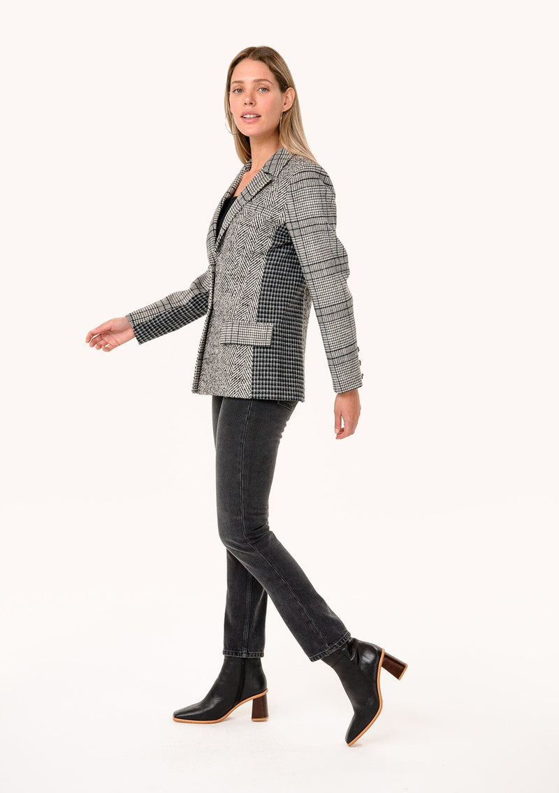 [Color: Cream/Black] A side facing image of a blonde model wearing a classic blazer in a grey patchwork plaid. With a button front, long sleeves, and side flap pockets. 
