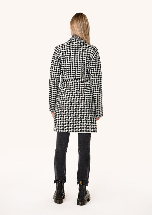 [Color: White/Black] A back facing image of a blonde model wearing a classic fall cardigan in a white and black houndstooth. With long sleeves, a shawl collar, side pockets, and a tie waist belt. 