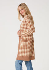 [Color: Taupe/Cream] A side facing image of a blonde model wearing a mid length fuzzy sweater coat in a brown and cream houndstooth plaid design. With long sleeves, an open front, and side patch pockets. 