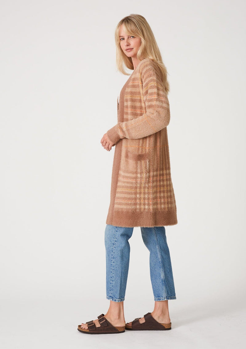 [Color: Taupe/Mustard] A side facing image of a blonde model wearing a fuzzy sweater coat in a brown plaid design. With long sleeves, an open front, a mid length hemline, and side patch pockets. 