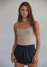 [Color: Light Taupe] A front facing image of a brunette model wearing a basic taupe cami with a stretchy, seamless fit and fixed spaghetti straps. 