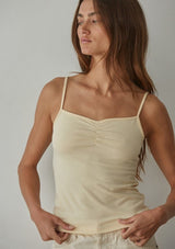 [Color: Buttermilk] A front facing image of a brunette model wearing a light yellow jersey cami with a ruched bust and spaghetti straps. 