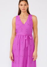 [Color: Orchid] A close up front facing image of a brunette model wearing a an orchid purple bohemian mid length dress made with embroidered eyelet. A sleeveless spring dress with a v neckline, a tiered skirt, an adjustable waist tie, and a back keyhole with button closure. 