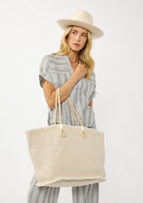 [Color: White/Natural] A blonde model holding a bohemian tote bag in a light beige texture. With stitched detail throughout, two rope handles, and a top zip closure.