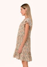 [Color: Cream/Teal] A side facing image of a blonde model wearing a lightweight fall mini dress in a cream and teal floral print. With short double flutter cap sleeves, a tiered skirt, a self covered loop button front, and a v neckline with ties. 