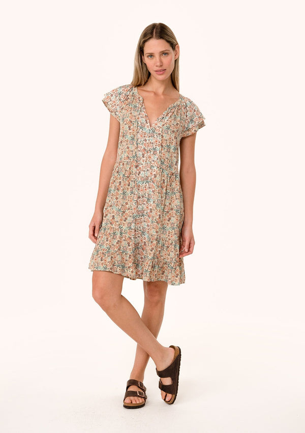 [Color: Cream/Teal] A front facing image of a blonde model wearing a lightweight fall mini dress in a cream and teal floral print. With short double flutter cap sleeves, a tiered skirt, a self covered loop button front, and a v neckline with ties. 
