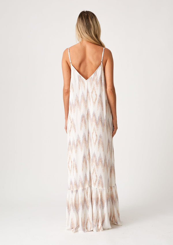 [Color: Natural/Taupe] A back facing image of a blonde model wearing a bohemian maxi tank dress in an off white and taupe chevron striped print. With a v neckline in the front and back, adjustable spaghetti straps, a tiered skirt, side pockets, and a flowy relaxed fit. 