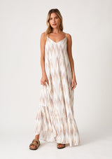 [Color: Natural/Taupe] A front facing image of a blonde model wearing a bohemian maxi tank dress in an off white and taupe chevron striped print. With a v neckline in the front and back, adjustable spaghetti straps, a tiered skirt, side pockets, and a flowy relaxed fit. 