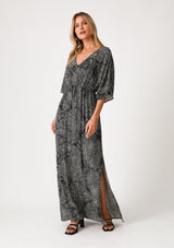 [Color: Black/Natural] A front facing image of a blonde model wearing a flowy bohemian maxi dress in a black floral print. With short sleeves, a v neckline, a long maxi skirt with side slits, and a drawstring waist with adjustable front tie. 