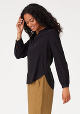 [Color: Black] A side facing image of a brunette model wearing a black blouse with a v neckline, long sleeves, a relaxed fit, and a smocked detail at the back.