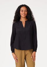 [Color: Black] A front facing image of a brunette model wearing a black blouse with a v neckline, long sleeves, a relaxed fit, and a smocked detail at the back.