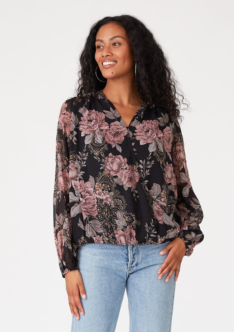 [Color: Black/Dusty Rose] A front facing image of a brunette model wearing a bohemian chiffon blouse designed in a black and pink floral print. With metallic details throughout, a surplice v neckline, long sleeves, and an elastic waist at the front. 