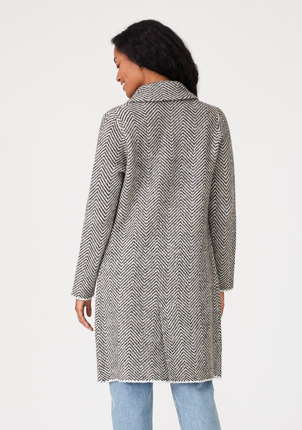 [Color: Taupe/Cream] A back facing image of a brunette model wearing a soft sweater coat in a taupe and cream herringbone pattern. With long sleeves, a button front, side pockets, a mid length hemline, and a notched collar. 