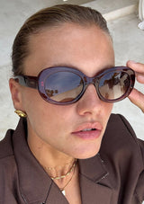 [Color: Dark Cherry] An image of a blonde woman wearing round sunglasses with a red frame from FREYRS.