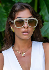 [Color: Grey Pearl] A woman wearing  sunglasses with a beige pearl frame from FREYRS.