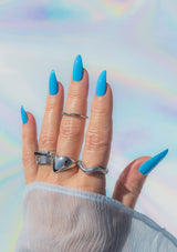 [Color: Coastal] Hand with blue nail polish and silver rings against a colorful, rainbow-patterned background