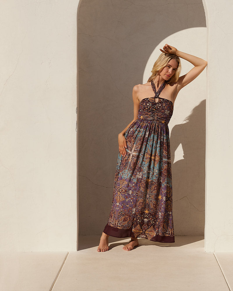 Lovestitch purple bohemian floral print halter maxi dress in a chic Moroccan print. Model is standing in front of a Spanish style resort doorway. The perfect vacation dress!
