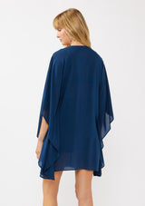 [Color: Navy] A back-facing image of a blonde model wearing a navy embroidered tunic mini dress, perfect as a beach cover-up. This sheer, flowy dress features a split v-neckline with tassel detail and cascading, flowy sleeves.