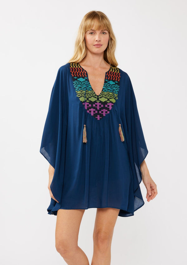 [Color: Navy] A front-facing image of a blonde model wearing a navy embroidered tunic mini dress, perfect as a beach cover-up. This sheer, flowy dress features a split v-neckline with tassel detail and cascading, flowy sleeves.