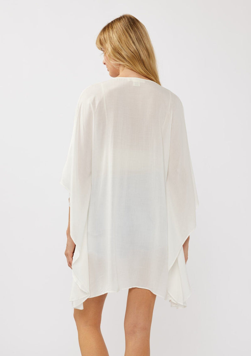 [Color: Off White] A back-facing image of a blonde model wearing a white embroidered tunic mini dress, perfect as a beach cover-up. This sheer, flowy dress features a split v-neckline with tassel detail and cascading, flowy sleeves.