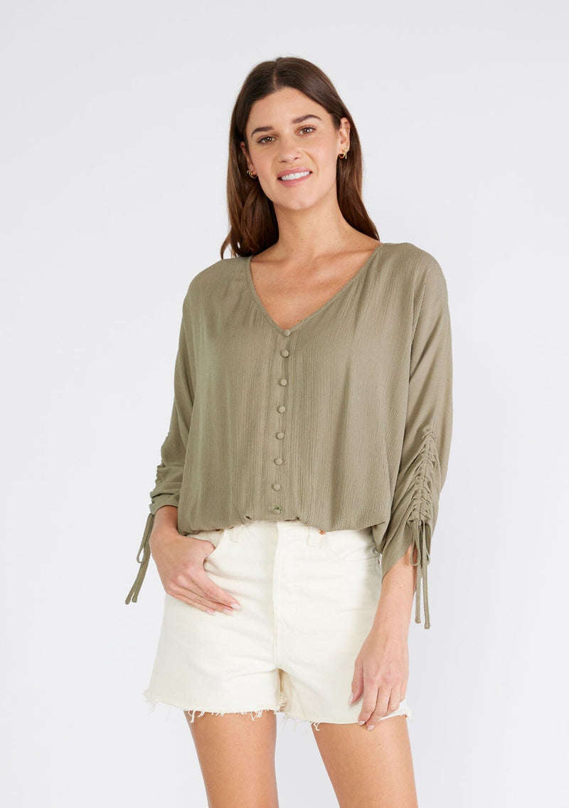 [Color: Olive] A front facing image of a brunette model wearing an olive green bohemian top. With a v neckline, a button front, an elastic waist, and three quarter length sleeves with adjustable ties. 