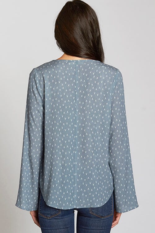 [Color: Slate Blue/Vanilla] A back facing image of a brunette model wearing a blue geometric print blouse with a lace up front, tassel detail, and flowy bell sleeves. 