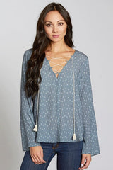 [Color: Slate Blue/Vanilla] A front facing image of a brunette model wearing a blue geometric print blouse with a lace up front, tassel detail, and flowy bell sleeves. 