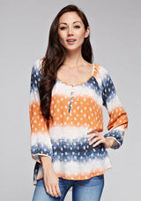 [Color: Coral/Navy] A brunette model wearing a tie dye blouse with paisley print in orange and blue. With a scoop neckline, long sleeves, and button front. A relaxed fit style paired with denim jeans. 