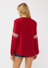 [Color: Red] A back facing image of a blonde model wearing a red embroidered boho peasant blouse with a split v-neckline, long sleeves, and tassel ties. 