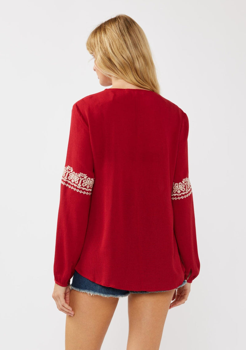 [Color: Red] A back facing image of a blonde model wearing a red embroidered boho peasant blouse with a split v-neckline, long sleeves, and tassel ties. 
