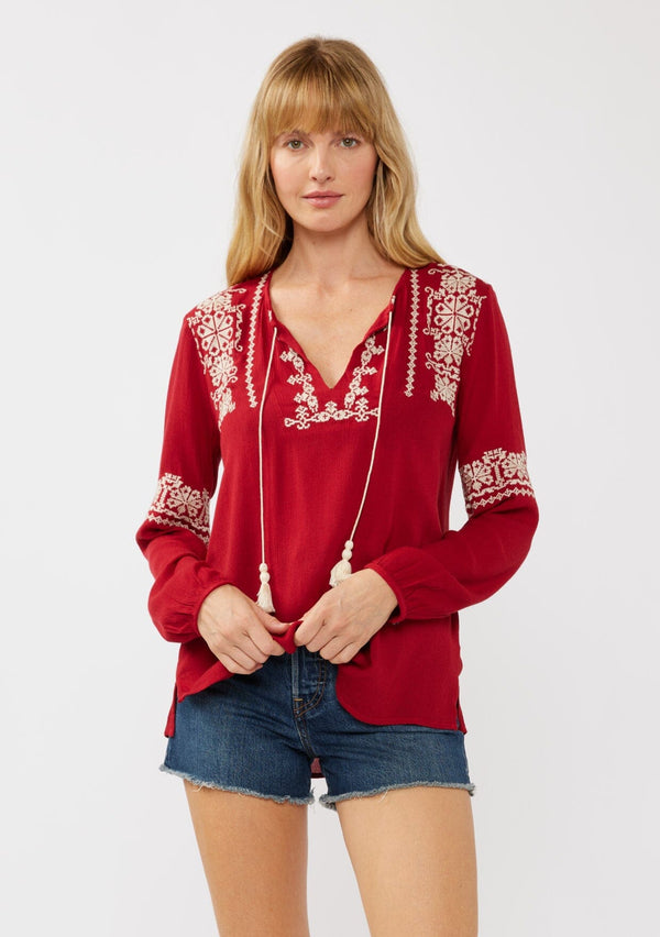 [Color: Red] A front facing image of a blonde model wearing a red embroidered boho peasant blouse with a split v-neckline, long sleeves, and tassel ties. 