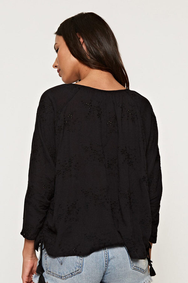 [Color: Black] A black facing image of a blonde model wearing a black blouse with embroidered details, split v-neckline, and a side tie detail. 