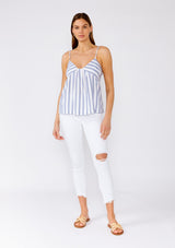 [Color: White/Blue] A full body front facing image of a brunette model wearing a classic warm weather camisole in a white and blue stripe. With adjustable spaghetti stripes, a v neckline, and a metallic gold stripe detail. 