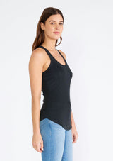 [Color: Black] A side facing image of a brunette model wearing a slim fit racerback tank top in black. With a scooped neckline and a raw edge hemline. 