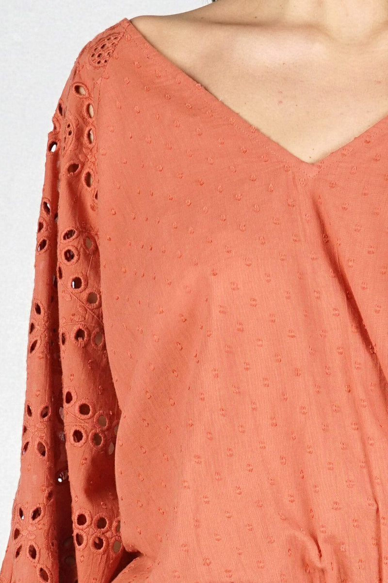 [Color: Terracotta] A detail image of a brunette model wearing a orange boho blouse with swiss dots and embroidered eyelet sleeves. Finished with a chic tie back detail and a comfortable elastic waistline. 