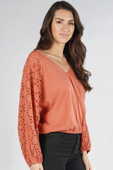 [Color: Terracotta] A front facing image of a brunette model wearing a orange boho blouse with swiss dots and embroidered eyelet sleeves. Finished with a chic tie back detail and a comfortable elastic waistline. 