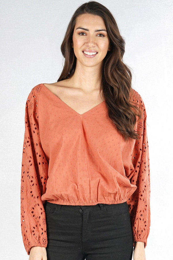 [Color: Terracotta] A front facing image of a brunette model wearing a orange boho blouse with swiss dots and embroidered eyelet sleeves. Finished with a chic tie back detail and a comfortable elastic waistline. 