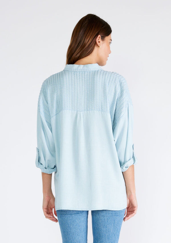[Color: Bleach Wash] A back facing image of a brunette model wearing a light blue wash Tencel shirt. With long three quarter length sleeves, a button tab sleeve, a collared neckline, a button front, two front patch pockets, and pintuck details. 