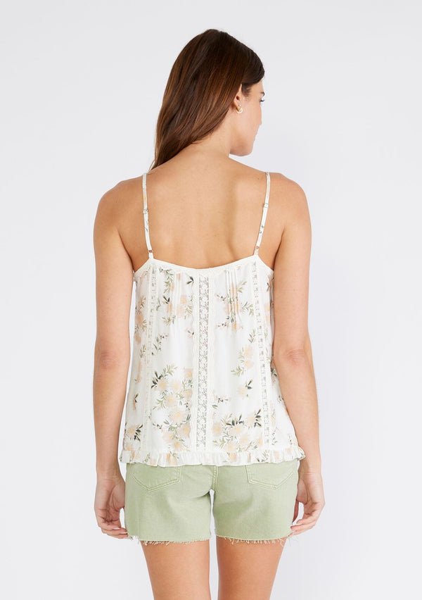 [Color: Ivory/Dusty Coral] A back facing image of a brunette model wearing a flowy bohemian camisole in an ivory and pink floral print. With adjustable spaghetti straps, a v neckline, lace trim, a ruffled hemline, and pintuck details. 