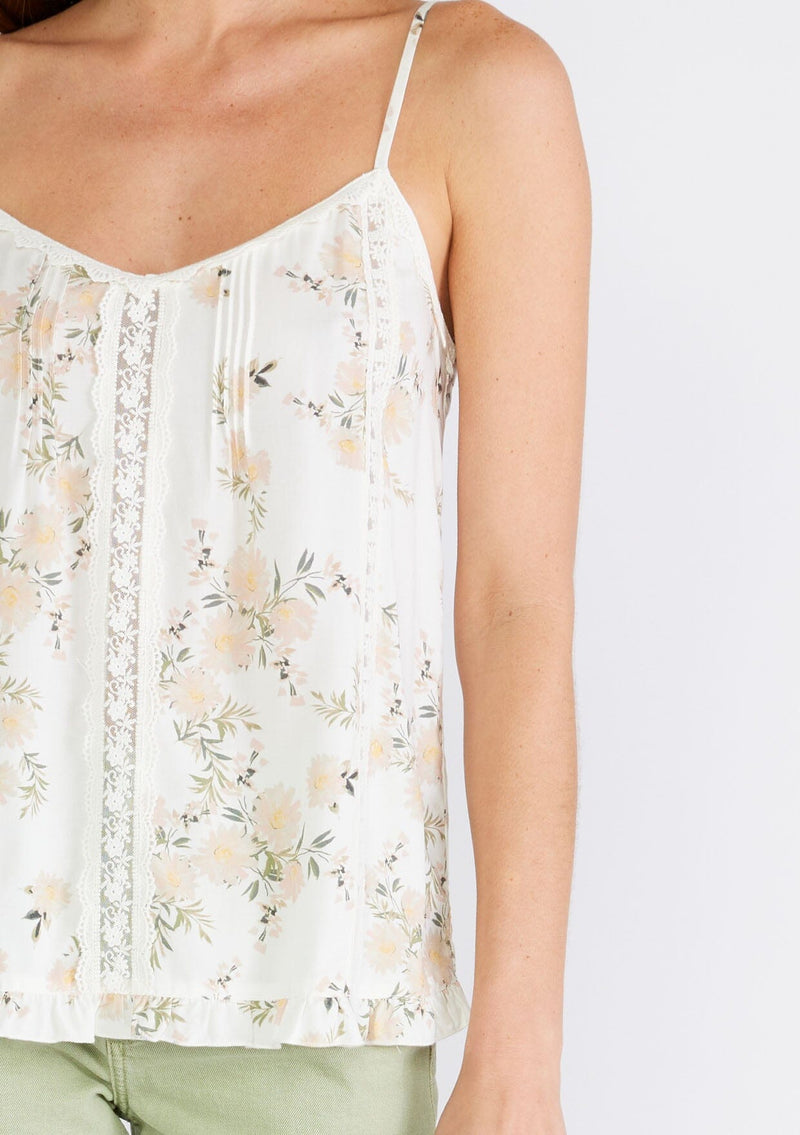 [Color: Ivory/Dusty Coral] A close up front facing image of a brunette model wearing a flowy bohemian camisole in an ivory and pink floral print. With adjustable spaghetti straps, a v neckline, lace trim, a ruffled hemline, and pintuck details. 